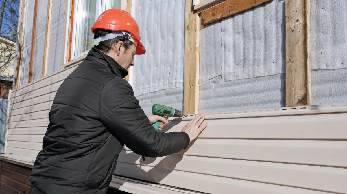 Siding replacement professional using a power drill to install new tan vinyl siding on a home exterior in Ann Arbor, Mi